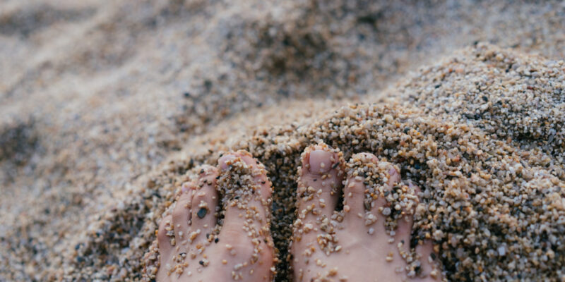 Woman's toes in the sand. Only the front 2/3 of the feet are in the image.